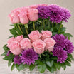 Pink roses and purple chrysanthemums arranged in a white wicker basket with green leaves