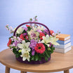 Mixed flower basket with white lilies, red gerbera daisies and purple carnations in a purple wicker basket with arched handle