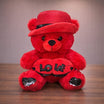 Red fluffy teddy bear wearing a red straw hat with black sequin band holding a red LOVE heart plush