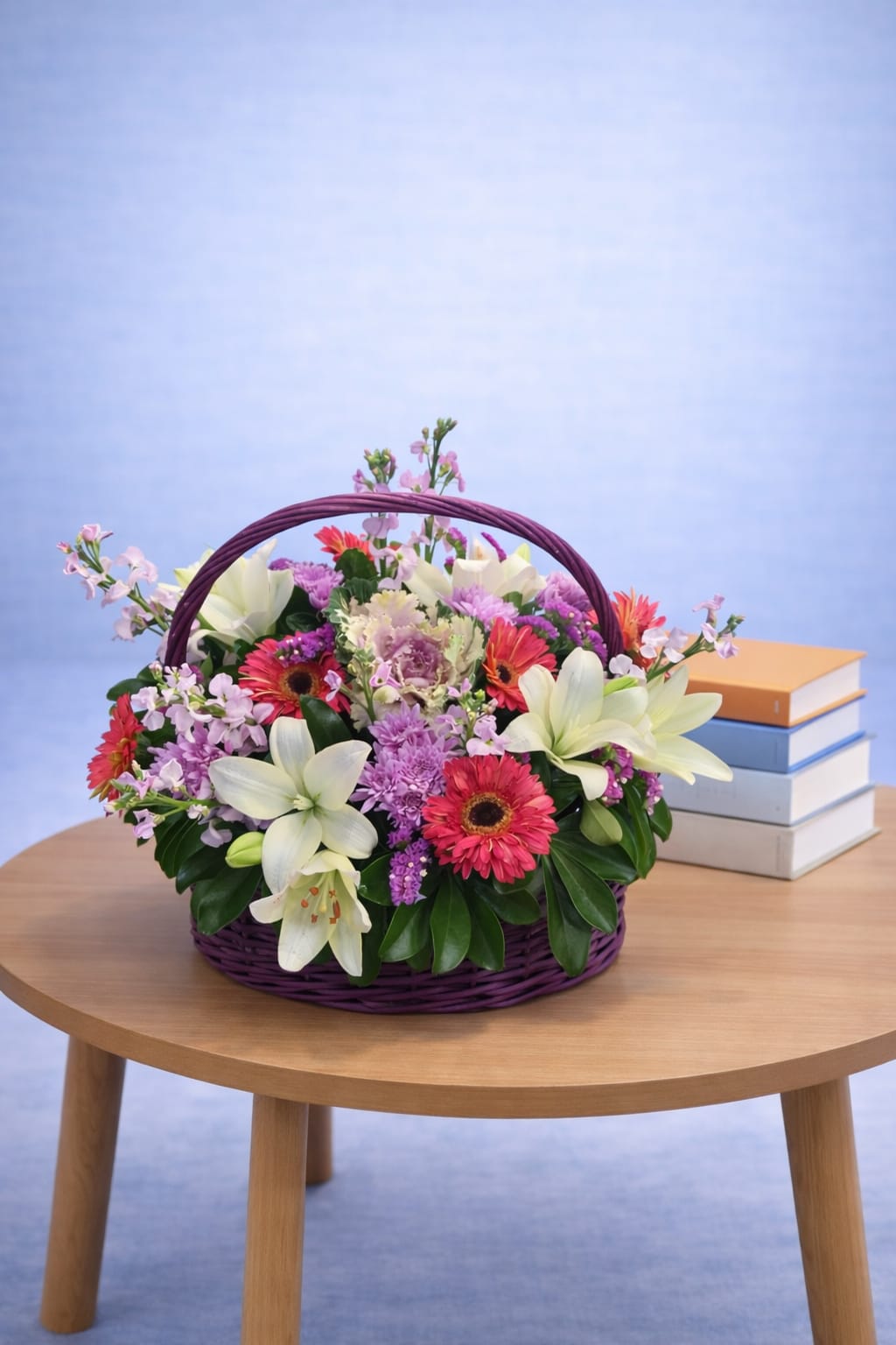 Mixed flower basket with white lilies, red gerbera daisies and purple carnations in a purple wicker basket with arched handle