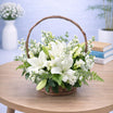 White oriental lily and stock flower arrangement in a natural wicker basket with arched handle and green fern leaves