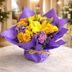 Yellow lily and orange chrysanthemum arrangement with purple statice wrapped in royal purple paper with raffia bow